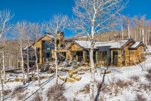 snow covered property featuring stone siding and a chimney