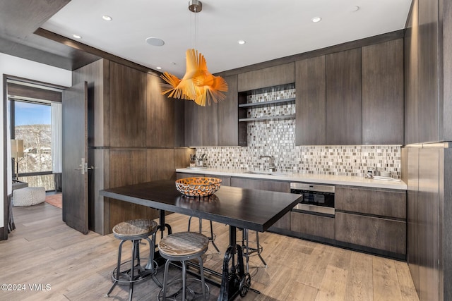 kitchen with dark brown cabinets, open shelves, light wood-type flooring, and a sink