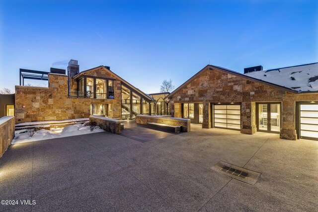 exterior space featuring french doors, a balcony, a garage, stone siding, and a patio