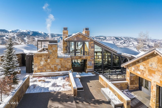 snow covered house with a mountain view, stone siding, and a chimney