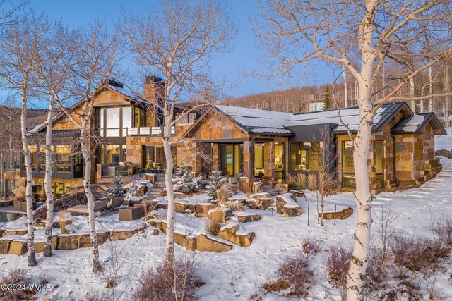 snow covered back of property with stone siding