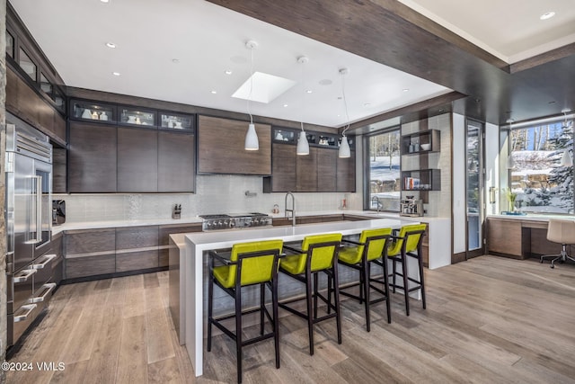 kitchen with light countertops, dark brown cabinets, light wood-type flooring, and a center island with sink