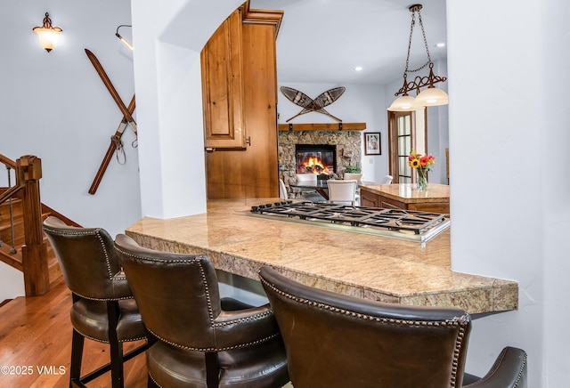 2241 Tahoe Dr, Vail, CO 81657 - kitchen with stainless steel gas stovetop, wood finished floors, a stone fireplace, a breakfast bar, and tile countertops