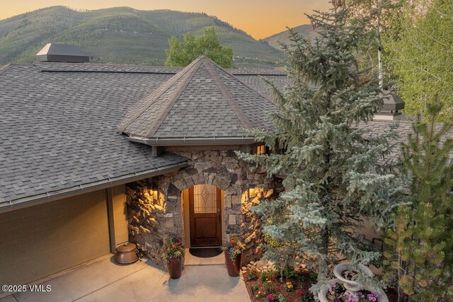 2241 Tahoe Dr, Vail, CO 81657 - exterior entry at dusk with roof with shingles, stone siding, and a mountain view