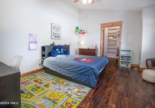 bedroom featuring baseboards, ceiling fan, wood finished floors, a walk in closet, and vaulted ceiling