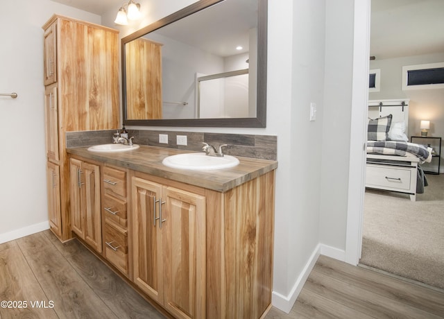 ensuite bathroom featuring baseboards, wood finished floors, a sink, and double vanity