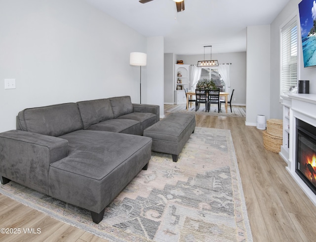 living area with a glass covered fireplace, light wood-type flooring, baseboards, and ceiling fan