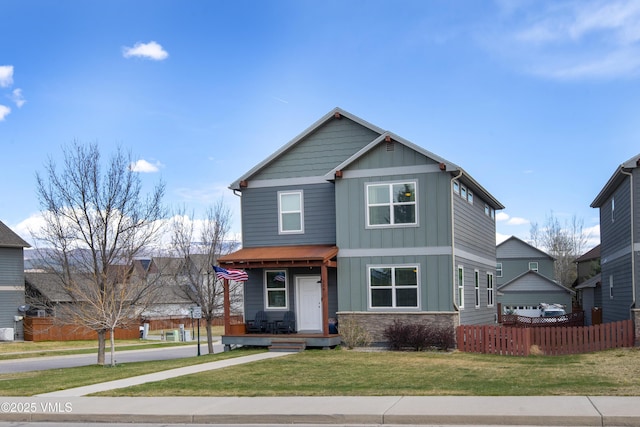 craftsman-style home with fence, board and batten siding, stone siding, a porch, and a front yard