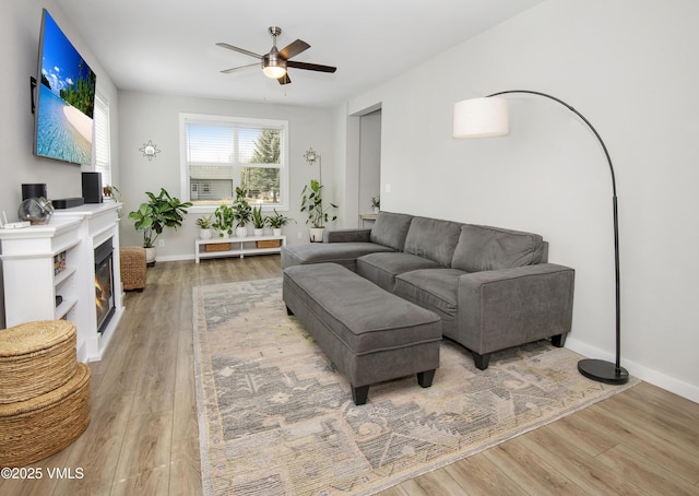 living area featuring light wood-style flooring, baseboards, and a ceiling fan