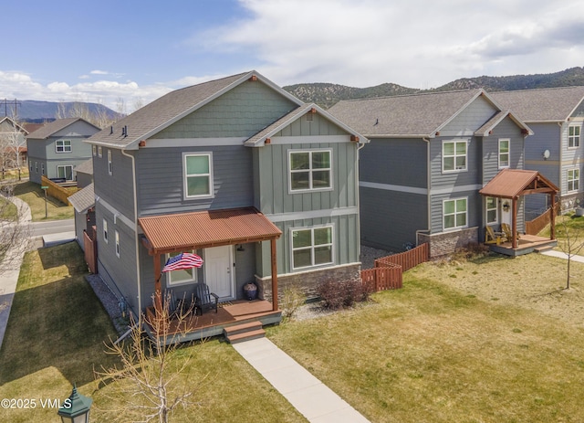 craftsman house featuring board and batten siding, stone siding, a front lawn, and a deck with mountain view