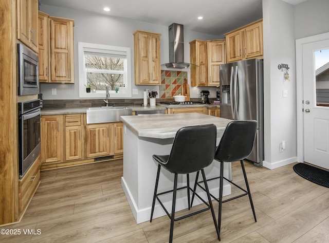 kitchen featuring wall chimney exhaust hood, stainless steel appliances, light wood-type flooring, and a sink