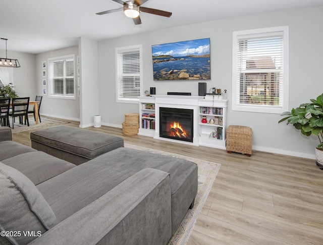 living room featuring wood finished floors, a glass covered fireplace, a ceiling fan, and baseboards