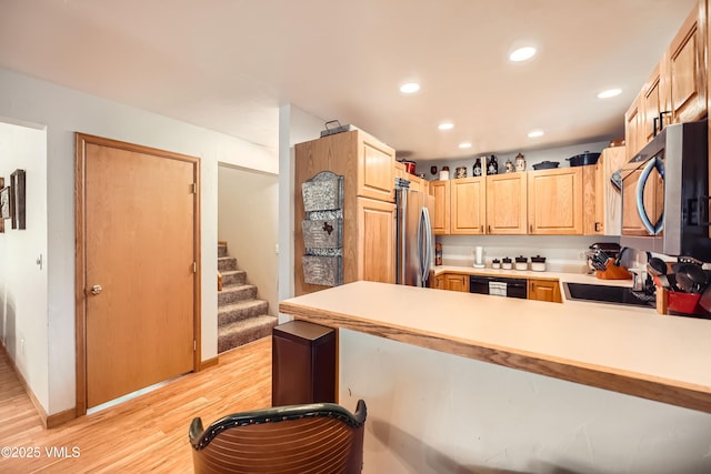 kitchen featuring appliances with stainless steel finishes, light brown cabinetry, light wood-type flooring, and kitchen peninsula