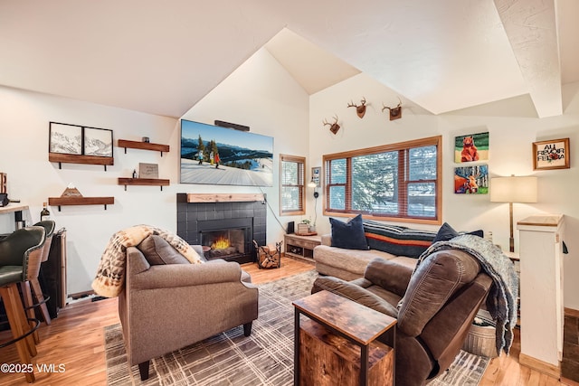 living room featuring high vaulted ceiling, a fireplace, and light hardwood / wood-style floors