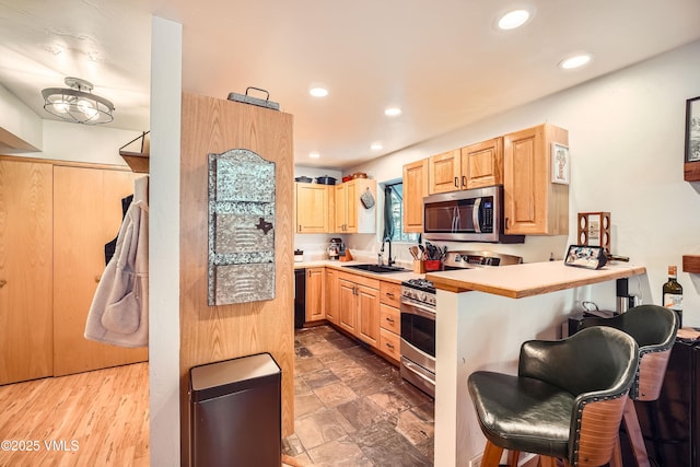 kitchen with light brown cabinetry, sink, stainless steel appliances, and a kitchen bar