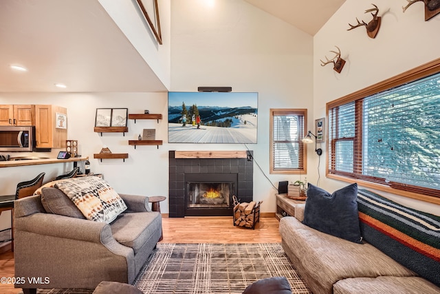 living room featuring high vaulted ceiling, light hardwood / wood-style flooring, and a tile fireplace