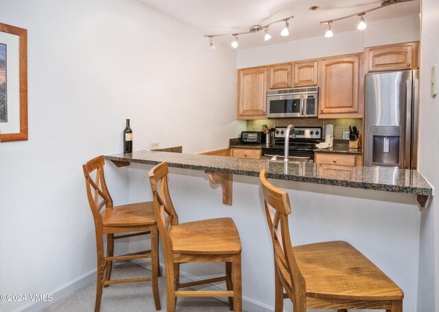 kitchen with a kitchen bar, appliances with stainless steel finishes, kitchen peninsula, dark stone counters, and backsplash