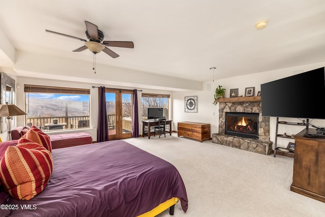 carpeted bedroom with access to outside, ceiling fan, and a stone fireplace