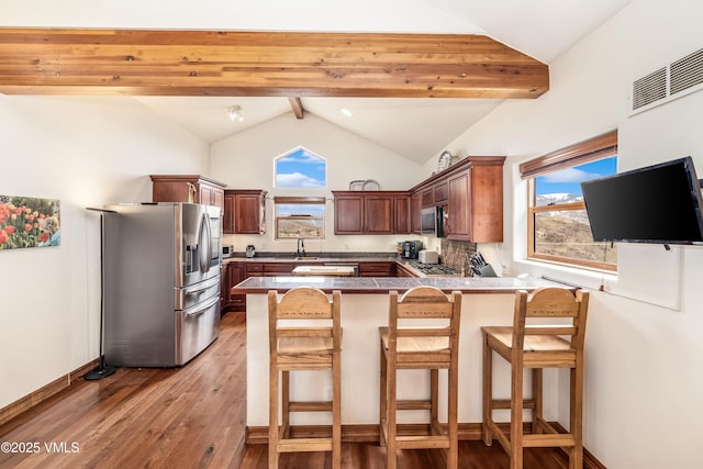 kitchen with a peninsula, a healthy amount of sunlight, lofted ceiling with beams, light wood-style flooring, and appliances with stainless steel finishes