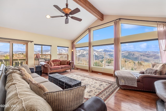 living area featuring beamed ceiling, ceiling fan, a wealth of natural light, and hardwood / wood-style floors
