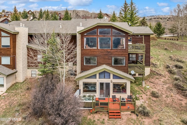 back of house featuring roof with shingles, a sunroom, a deck, a chimney, and a balcony