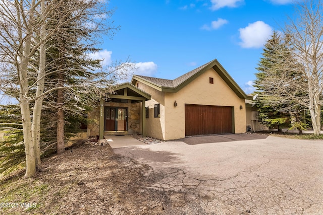 ranch-style home with an attached garage, driveway, stucco siding, and stone siding