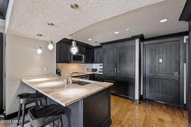 kitchen with a kitchen bar, sink, light wood-type flooring, kitchen peninsula, and pendant lighting