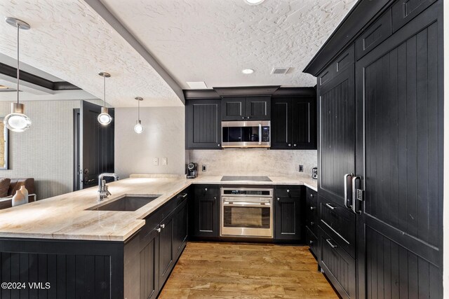 kitchen featuring appliances with stainless steel finishes, pendant lighting, sink, kitchen peninsula, and light wood-type flooring