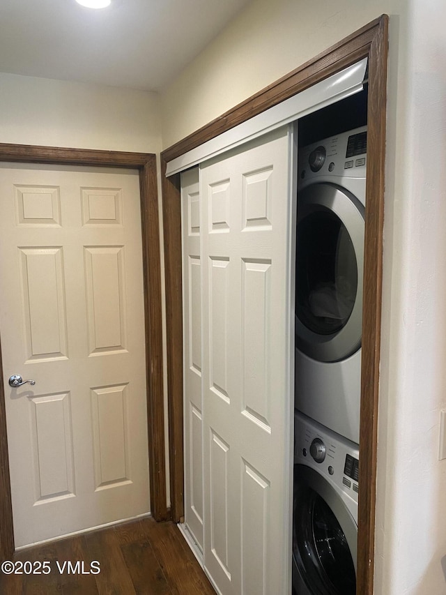 laundry room featuring stacked washer and dryer and dark wood-type flooring