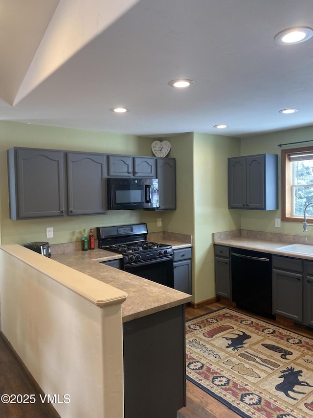 kitchen with sink, gray cabinets, black appliances, dark hardwood / wood-style flooring, and kitchen peninsula