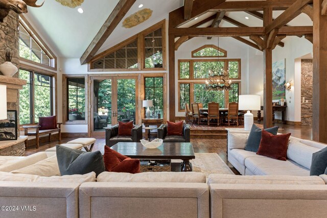 living room featuring an inviting chandelier, hardwood / wood-style floors, high vaulted ceiling, a stone fireplace, and beamed ceiling