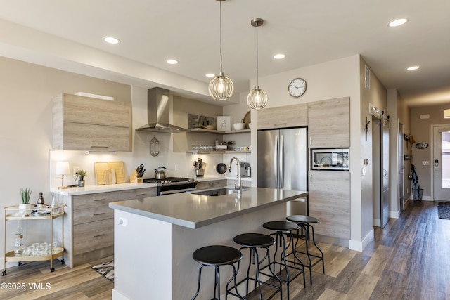 kitchen featuring modern cabinets, a sink, stainless steel appliances, a breakfast bar area, and wall chimney exhaust hood