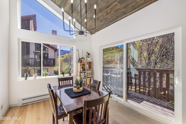 dining area with baseboard heating, wood finished floors, a chandelier, and a high ceiling