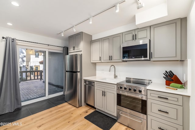 kitchen featuring stainless steel appliances, a sink, gray cabinets, track lighting, and light wood finished floors