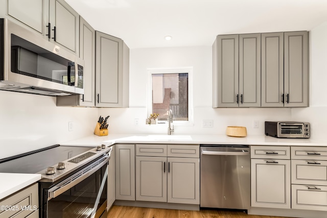 kitchen with appliances with stainless steel finishes, gray cabinetry, a sink, and recessed lighting