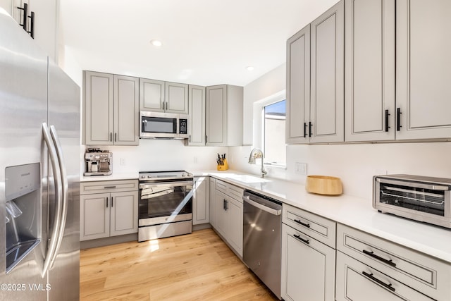 kitchen with appliances with stainless steel finishes, a sink, gray cabinetry, light wood-type flooring, and light countertops