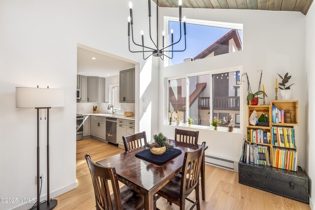 dining room with baseboard heating, light wood-style flooring, a chandelier, a high ceiling, and recessed lighting