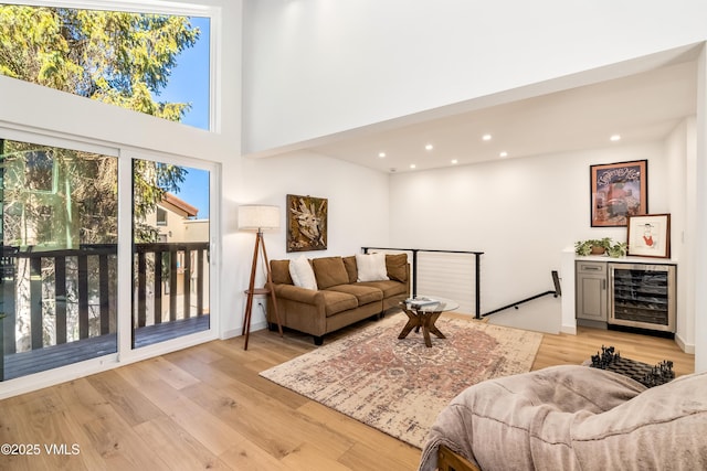 living room featuring beverage cooler, light wood-type flooring, a high ceiling, and recessed lighting