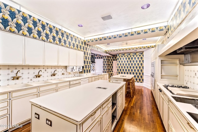 kitchen with a center island with sink, light countertops, dark wood-style floors, white appliances, and a sink