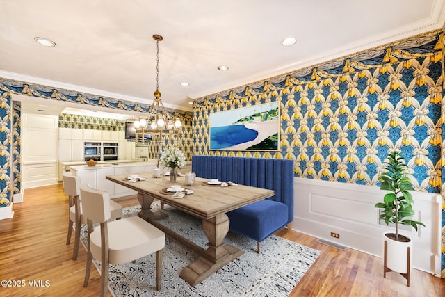 dining area with a decorative wall, wainscoting, light wood-type flooring, and crown molding