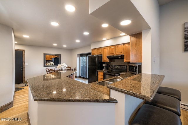 508 E Lionshead Cir Unit 502, Vail, CO 81657 - kitchen with black appliances, under cabinet range hood, light wood-style flooring, dark stone counters, and brown cabinetry