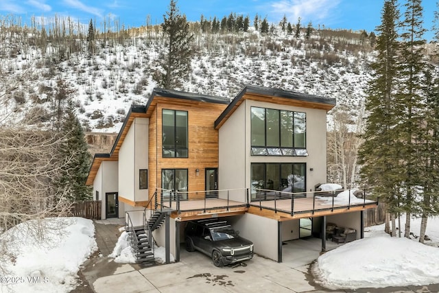 snow covered rear of property with stairway, a deck, and stucco siding