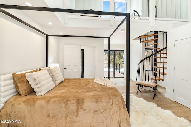 bedroom with a towering ceiling, access to exterior, wood finished floors, and recessed lighting