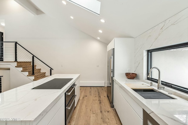 kitchen featuring black electric stovetop, light wood-style flooring, white cabinets, a sink, and stainless steel refrigerator