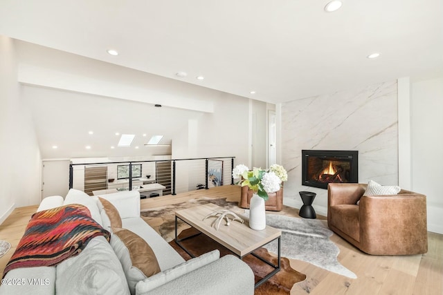 living area featuring light wood-type flooring, a skylight, a premium fireplace, and recessed lighting