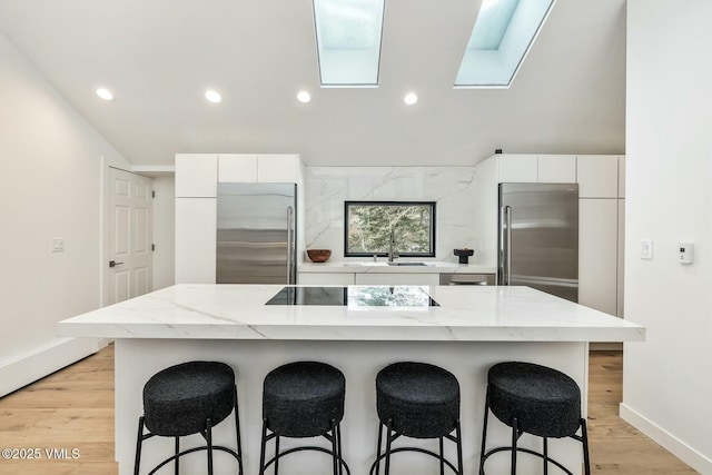 kitchen with white cabinets, light wood-style flooring, high quality fridge, stainless steel refrigerator, and a kitchen breakfast bar