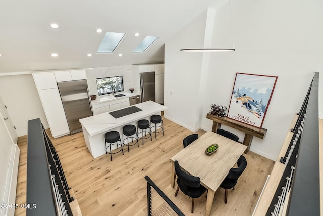 kitchen with appliances with stainless steel finishes, white cabinetry, a kitchen island, light wood-type flooring, and a kitchen bar