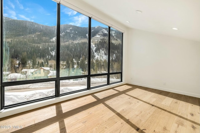 unfurnished room with a wall of windows, baseboards, a mountain view, and hardwood / wood-style floors