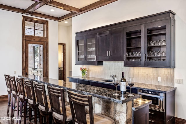 bar featuring decorative backsplash, oven, dark brown cabinetry, and dark stone counters