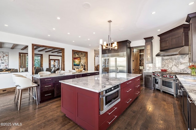 kitchen featuring hanging light fixtures, light stone counters, premium appliances, tasteful backsplash, and a kitchen island